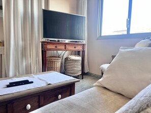 A living room with a television on a wooden stand, a sofa, a table with a remote, and two wicker baskets. - Riviera Beauty, Sun & Sea 80 m² close to the Mediterranean 4 pers, Clim, Pkg (Cagnes-sur-Mer)