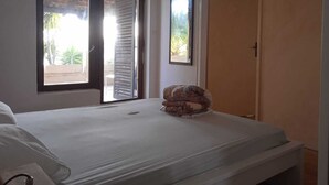 Un dormitorio con cama, ventana con persianas, puerta y vista a zonas verdes.