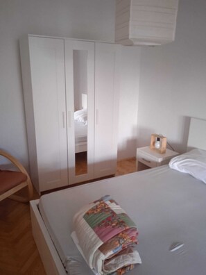 A bedroom with a bed, a wardrobe, a nightstand, and a chair.