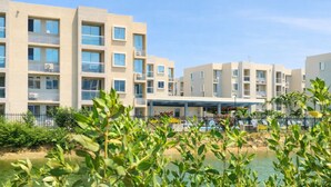 Um moderno conjunto de apartamentos com várias varandas, uma  área externa coberta e um corpo d'água em primeiro plano.