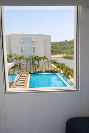 A pool with lounge chairs and palm trees, a building with windows, and a view of a beach and water. - The Colombian Dream in Cartagena, Modern 2-bed, 2-bath apartment + home office (Bolivar)