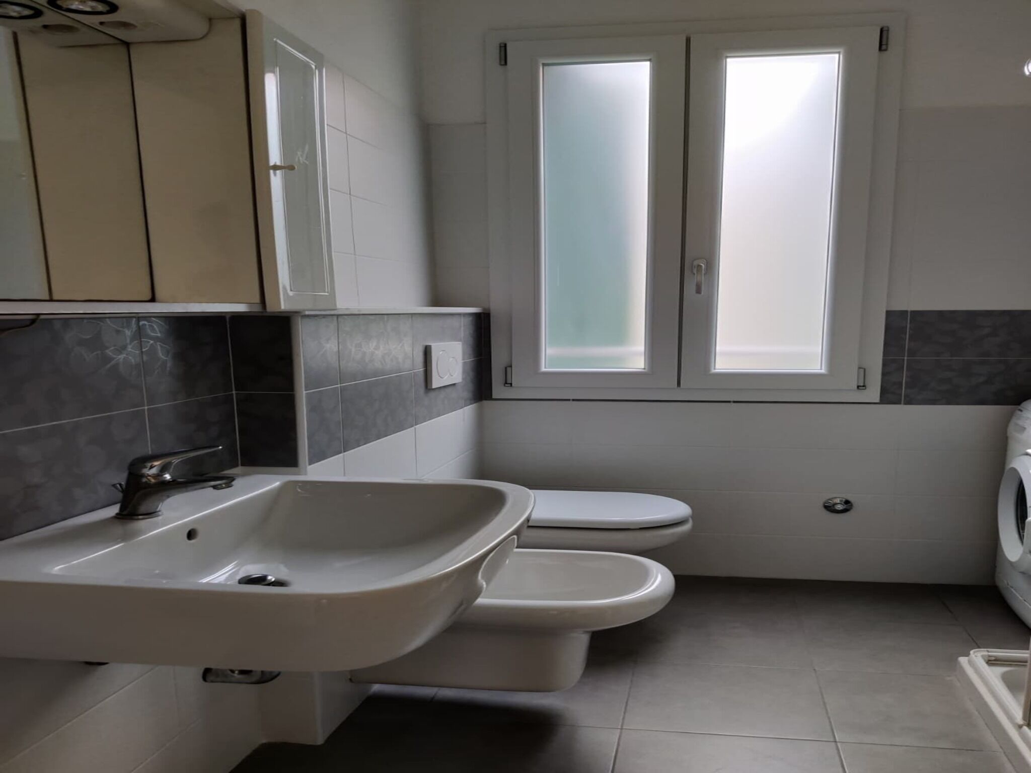 Een badkamer met een wastafel, twee toiletten en een raam.