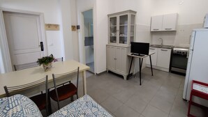 A compact kitchen with white cabinets, a dining table with chairs, a small TV on a stand, and a refrigerator. - Comfortable Property Seafront in Caorle (Caorle)