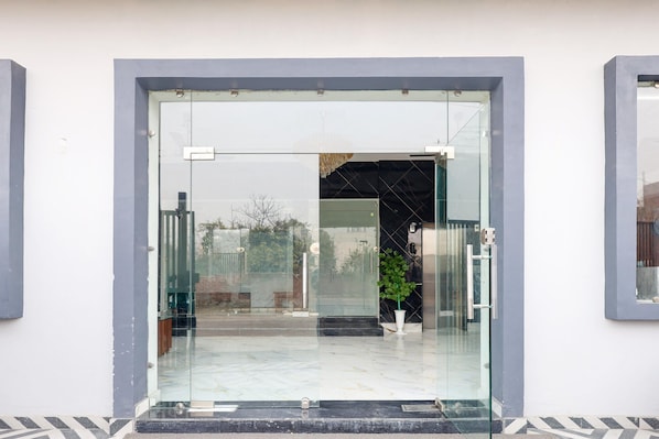 A modern entrance with a glass door, a potted plant, and a metal gate.