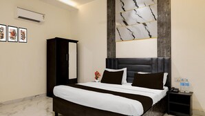 A hotel room with a large bed, a dark headboard, a nightstand with a phone and water bottles, and a wall-mounted air conditioner. - Premium GT Road Amritsar (Amritsar)
