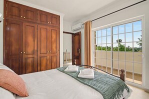 Une chambre dotée d’une grande armoire, d’un lit avec du linge de lit blanc, d’un plaid vert et donnant sur un paysage que l’on peut admirer à travers une porte-fenêtre coulissante.
