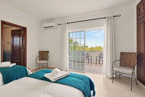 A hotel room with two beds, a balcony with a view, and a chair.