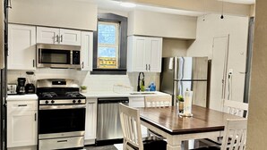 A modern kitchen with white cabinets, stainless steel appliances, a dining table with chairs, and a ceiling fan.