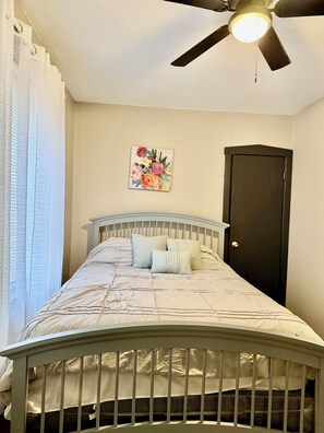 Une chambre à coucher avec un lit, un ventilateur de plafond, une porte et une œuvre d’art à motifs floraux accrochée au mur.