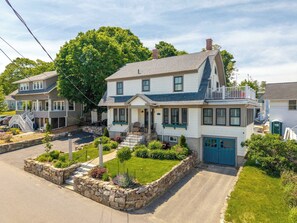 A two-story house with a front porch, a stone retaining wall, and a small garden. - Casa sul Mare Near the Coast (Ogunquit)