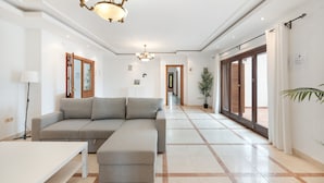 A modern living room with a grey sectional sofa, a white coffee table, and a chandelier. - Villa 'Mirador' con piscina compartida, Wi-Fi y aire acondicionado (Coín)