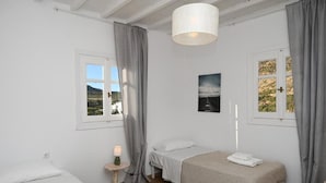 A bedroom with two beds, a bedside table with a lamp, a window with curtains, and a picture on the wall. - MZ Mykonos Rock (Mykonos)