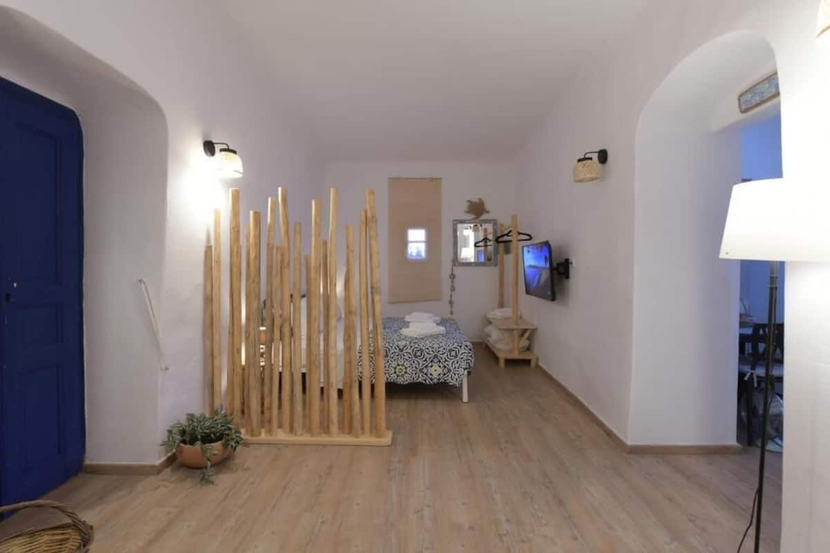 Una habitación con cama, televisor, un panel de madera y una lámpara.