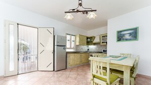 A kitchen with a dining area, a refrigerator, cabinets, and a painting on the wall. - Sardinian Apartment for 6 with Private Terrace, Three Minutes’ Walk from the Beach (Orosei)