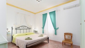 A bedroom with a bed, a chair, a nightstand, and an air conditioning unit. - Sardinian Apartment for 6 with Private Terrace, Three Minutes’ Walk from the Beach (Orosei)