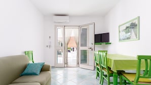 A room with a sofa, a dining table with chairs, a TV, and a door leading outside. - Sardinian Apartment with Private Terrace 3 Minutes’ Walk from the Beach (Orosei)