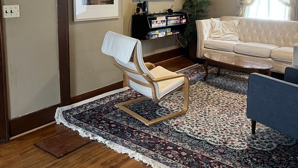 A living room with a wooden floor, a white sofa, a blue armchair, a patterned rug, a television, and a ceiling fan. - Serene 3-bedroom house in charming Syracuse (Syracuse)