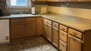 A kitchen with wooden cabinets, a sink, a dishwasher, and a window with curtains. - Serene 3-bedroom house in charming Syracuse (Syracuse)