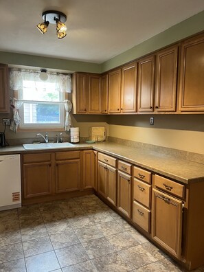 A kitchen with wooden cabinets, a sink, a dishwasher, and a window with curtains. - Serene 3-bedroom house in charming Syracuse (Syracuse)