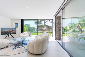 Una sala de estar moderna con un gran ventanal que da a un jardín, una mesa de centro redonda y un sofá confortable.