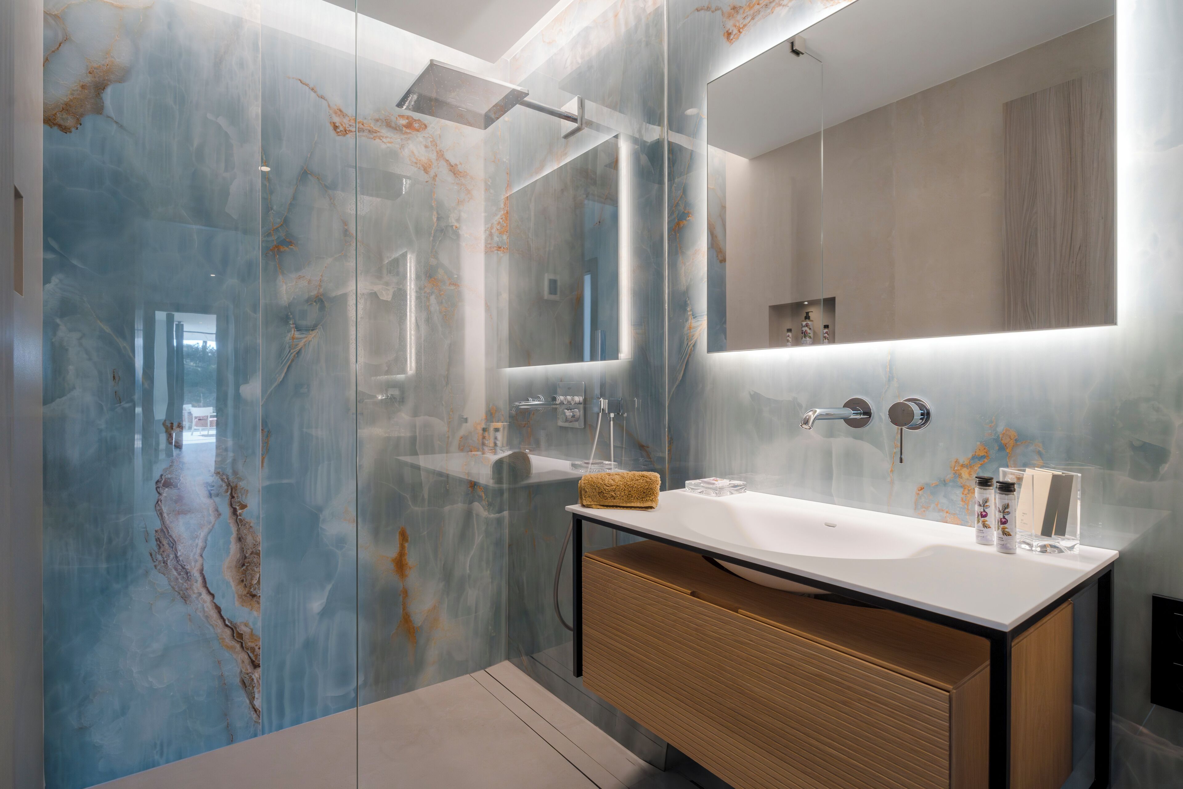 Une salle de bain moderne avec un mur en marbre, un lavabo blanc, un meuble-lavabo en bois et un miroir.
