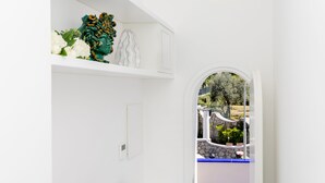 Un pasillo estrecho con paredes blancas, un tragaluz circular pequeño y vistas a un balcón exterior con barandilla azul.