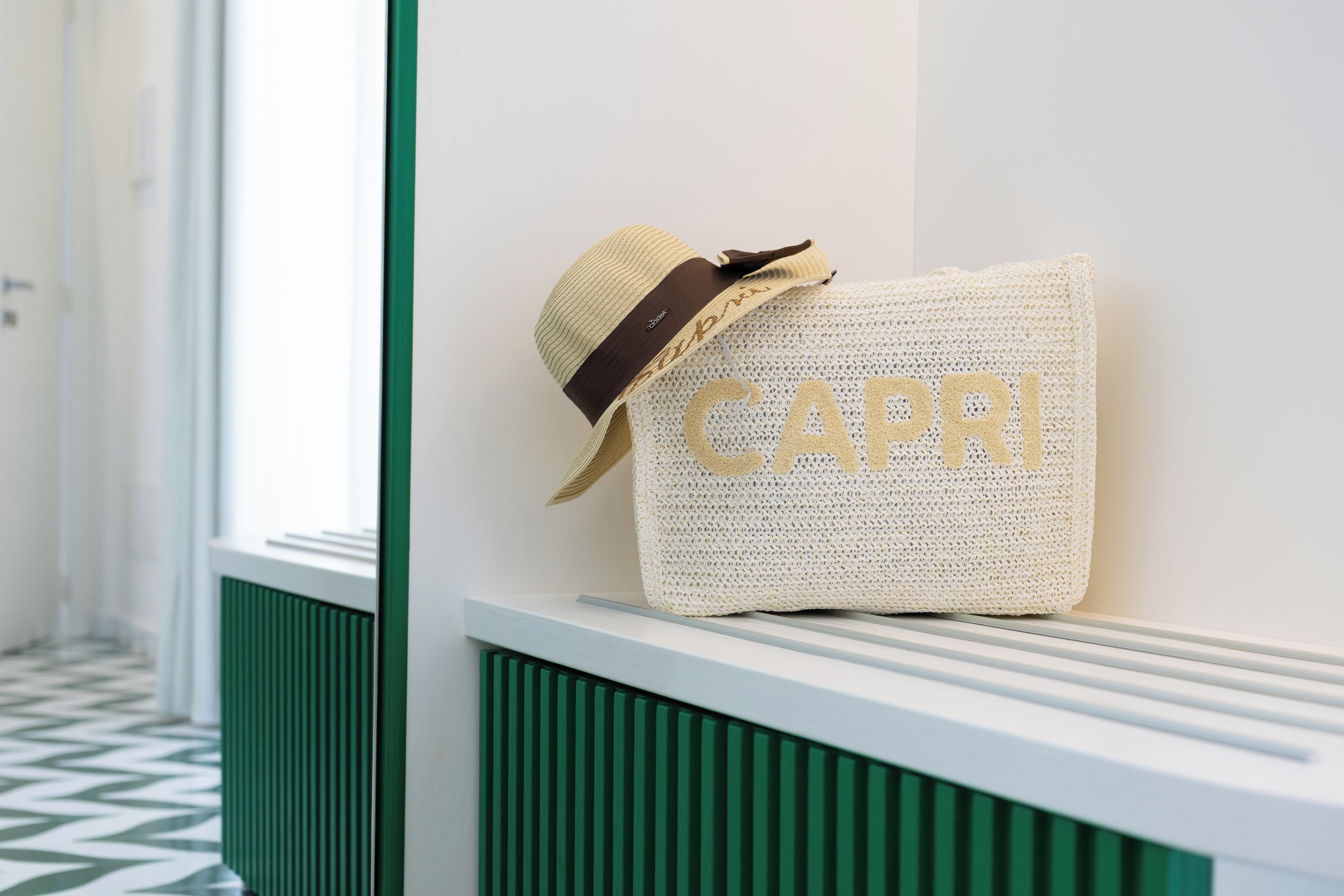Un chapeau orné du mot « CAPRI » et un sac tressé, posés sur un banc blanc.