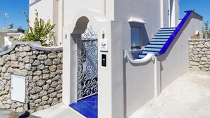 Una casa moderna de dos pisos con un muro de piedra, entrada con azulejos azules y una escalera que conduce al piso superior.