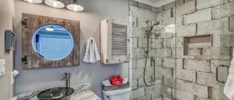 A bathroom with a glass-enclosed shower, a round mirror, and a marble sink.