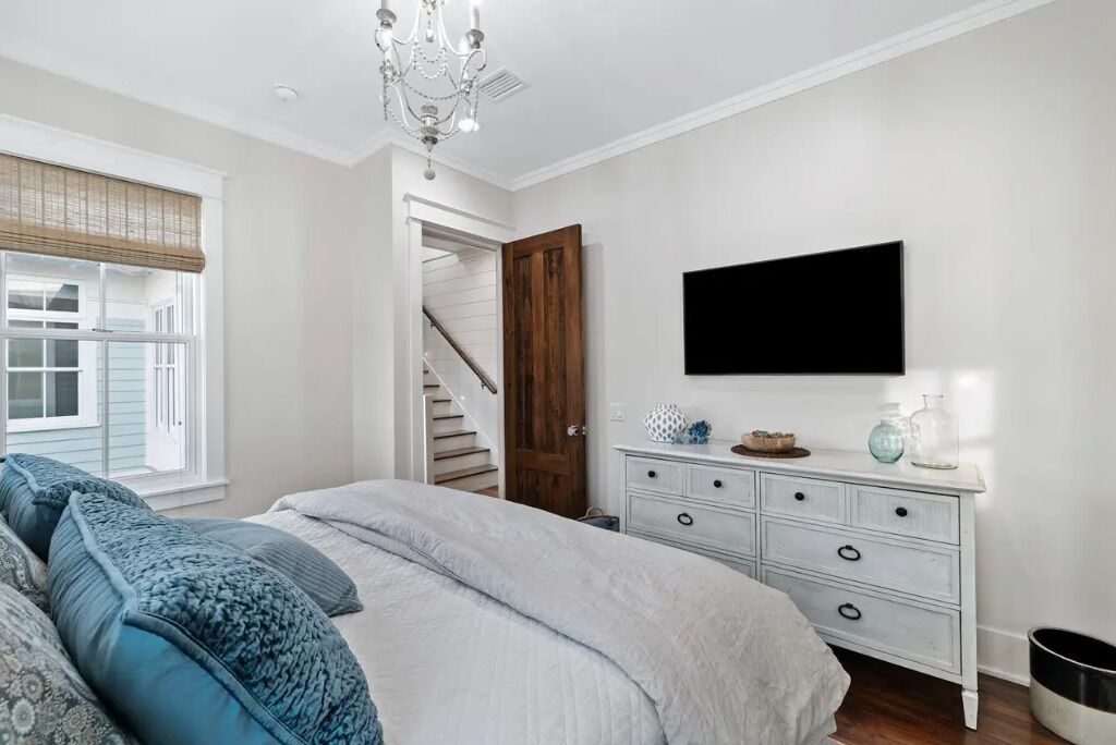 A bedroom with a bed, a dresser, a TV mounted on the wall, and a staircase leading to another room.