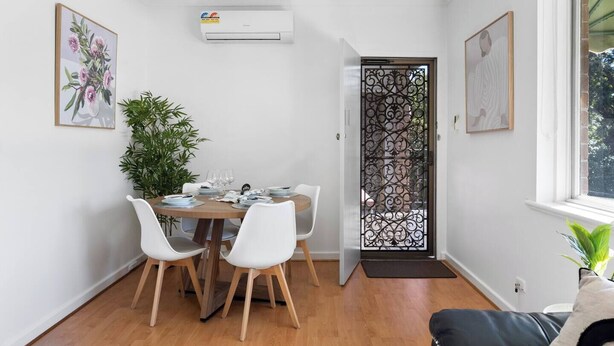 Ein Essbereich mit einem Tisch für vier Personen, weißen Stühlen, einem Blumentopf und einer Klimaanlage an der Wand.