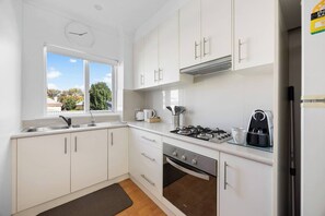 Una cocina moderna con armarios blancos, estufa a gas, cafetera y un reloj en la pared.