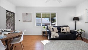 Ein modernes Wohnzimmer mit Essbereich, Deckenventilator, Fenster mit Aussicht und einer schwarzen Couch mit dekorativen Kissen.