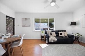 Una sala de estar moderna con comedor, ventilador de techo, ventana con vistas y un sofá negro con almohadones decorativos.