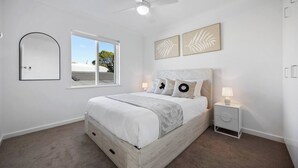 Ein Schlafzimmer mit Bett, Nachttisch, Deckenventilator, Fenster und Wandbildern.