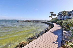 A wooden boardwalk leading to a pier extending into the water, with a building and palm trees nearby. - Sanibel Waterfront 3BR | Dock, Pool, Pickleball (Sanibel)