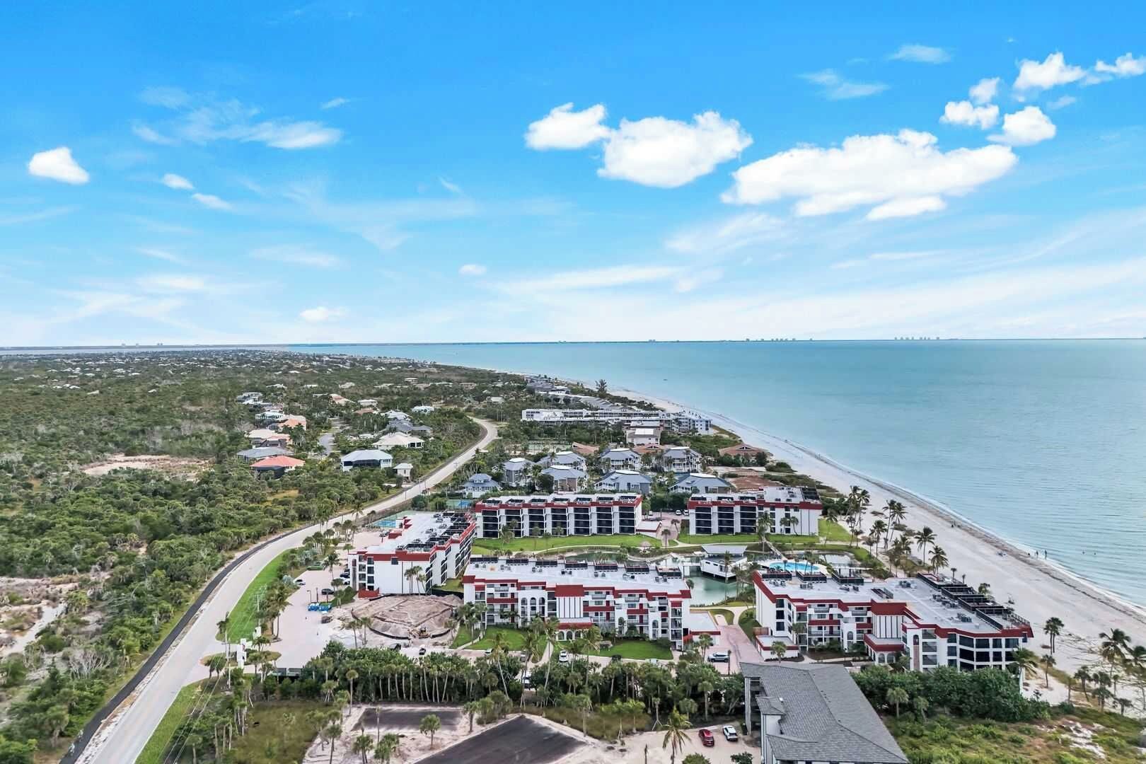 A coastal hotel with multiple buildings, a beach, and a clear sky.