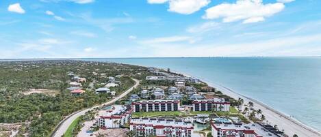 A coastal hotel with multiple buildings, a beach, and a clear sky.