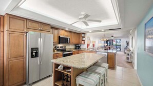 Una cocina moderna con armarios de madera, electrodomésticos de acero inoxidable, encimera de granito y ventilador de techo.