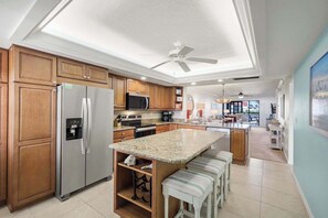 A modern kitchen with wooden cabinets, stainless steel appliances, a granite countertop, and a ceiling fan.