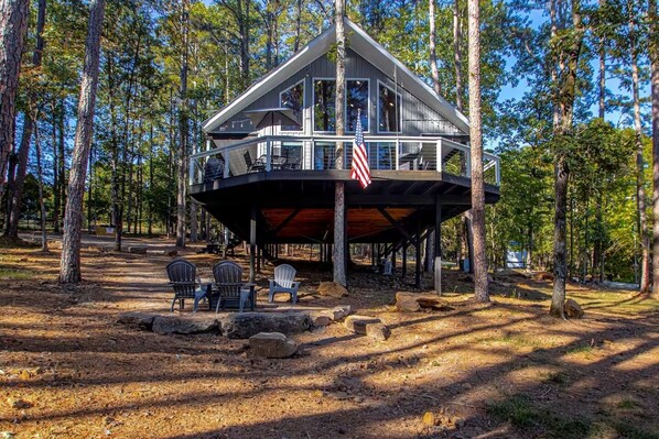 A two-story cabin with a deck, surrounded by trees. - Dogwood Den Treehouse Cabin in Shirley, AR at Greers Ferry Lake (Edgemont)