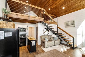 A modern interior with a wooden staircase, a kitchen area, and a living space with a sofa. - Dogwood Den Treehouse Cabin in Shirley, AR at Greers Ferry Lake (Edgemont)