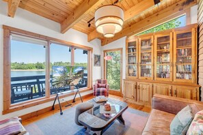 A spacious room with large windows, a wooden ceiling, a cozy seating area, and a bookshelf.