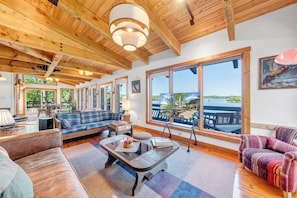 Un salon spacieux doté d’une grande fenêtre, de poutres apparentes en bois et offrant une vue sur un lac.