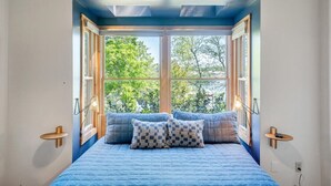Una camera da letto con un'ampia finestra, un letto con biancheria azzurra e due abat-jour.