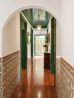 A hallway with tiled walls, a stone wall at the end, and a wooden counter with a vase of flowers. - An Encantada | Spa & Vista 180° | Casa de Artista (Alqueve - Folques)