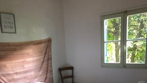 Un letto singolo con struttura in legno, una sedia, una finestra vista alberi e una citazione incorniciata al muro.