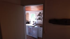 Un corridoio stretto che porta a una cucina con mobili bianchi, un lavandino e una finestra.