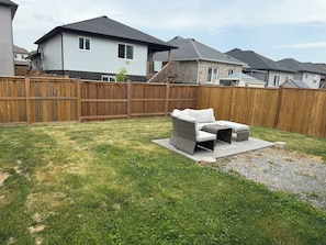 A backyard with a patio area, a wooden fence, and houses in the background.