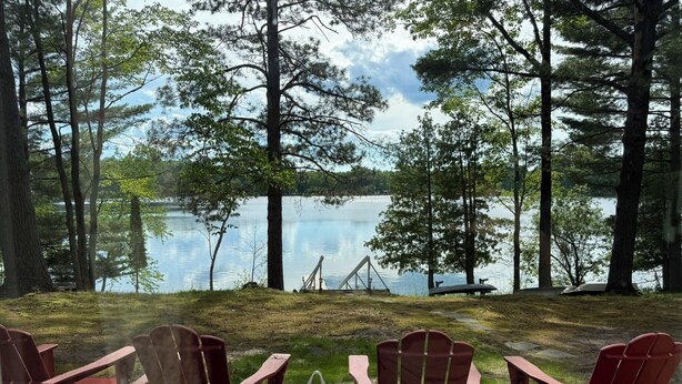 Blick auf einen See mit roten Adirondack-Stühlen und einem Glastisch, umgeben von Bäumen.
